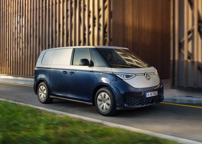 Blue and white electric van driving next to a wooden building