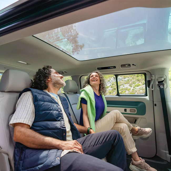 Two people sitting in the rear of a van with a sunroof above them