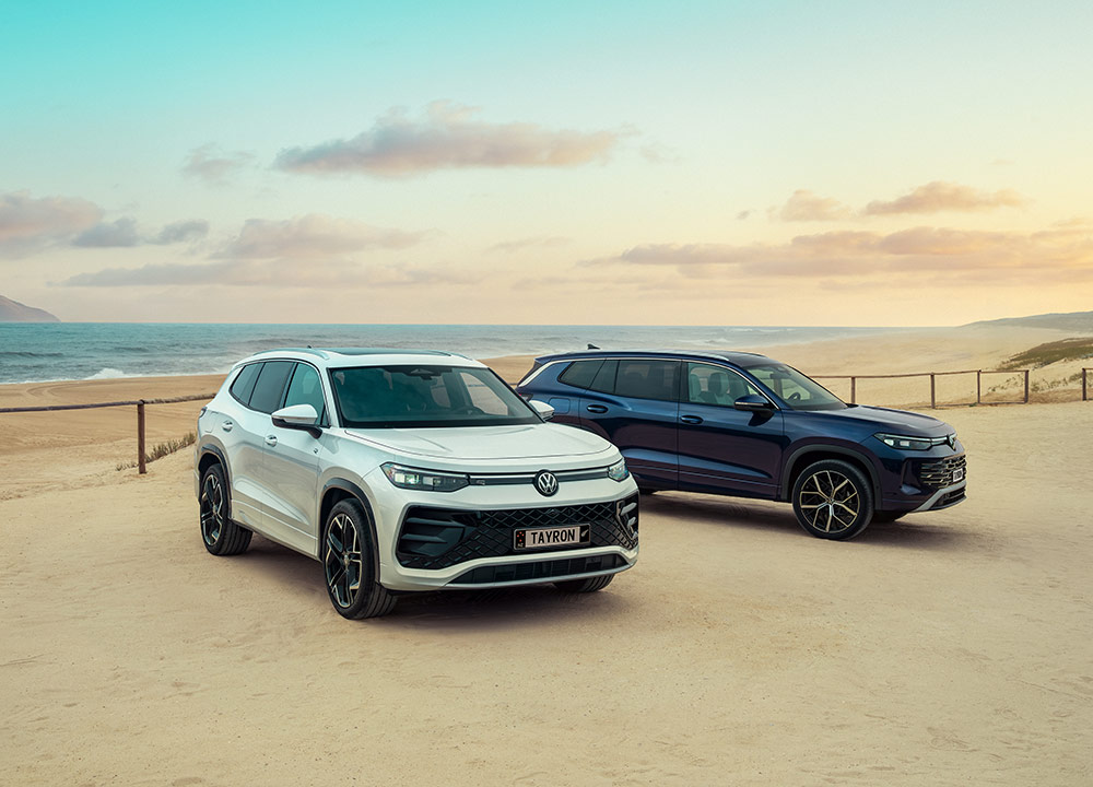 A silver SUV next to a blue SUV, parked next to a beach